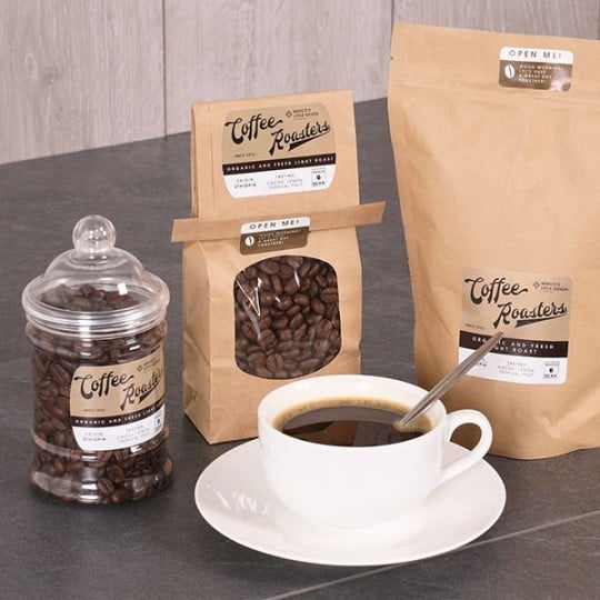 embalagens de café de papel e potes de vidro com etiquetas adesivas indicando o produto. xícara de café branca no centro