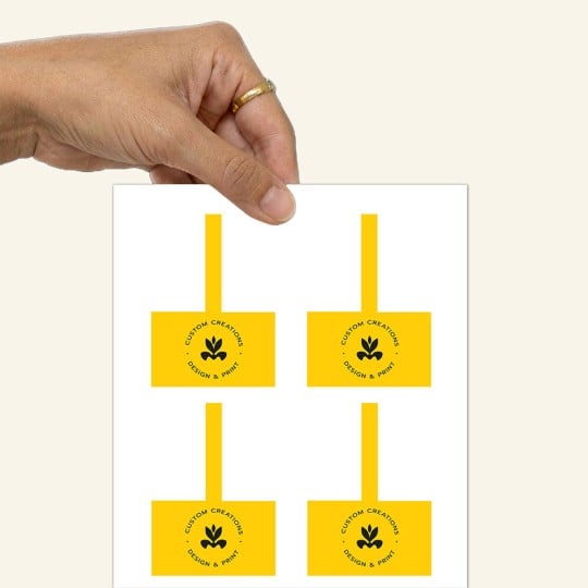 Uma mão que segura uma cartela de etiquetas retangulares pretas para potes.