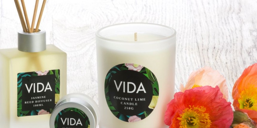 Aromatizador de ambiente branco vela e pequeno frasco com a etiqueta "VIDA wax candle" anexada Flores ao redor como decoração