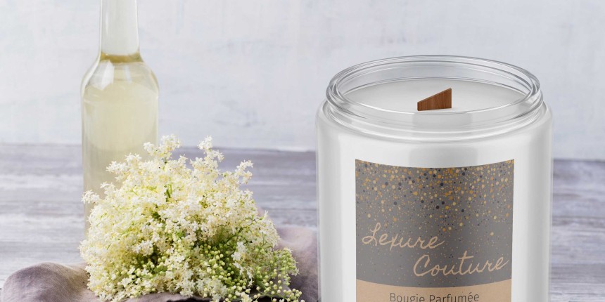 Vela em frasco de vidro com etiqueta cinza na frente. Decorações com flores ao redor