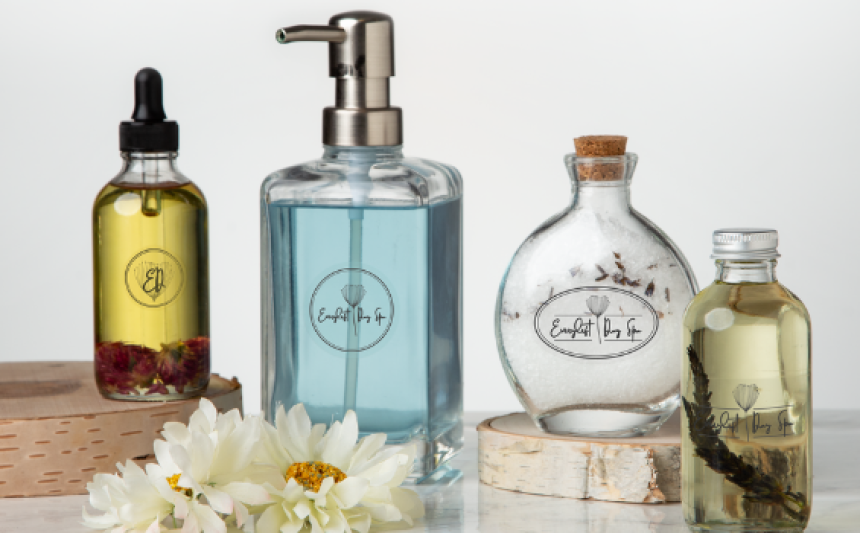 Quatro garrafas de vidro contendo sabão ou cosméticos com etiquetas transparentes. Decoração com flores ao redor