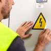 Trabalhador colando etiqueta adesiva triangular amarela com indicação de corrente elétrica no painel elétrico