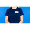 Mulher com camiseta azul e cracha adesivo seda de acetato retangular indicando nome e função.